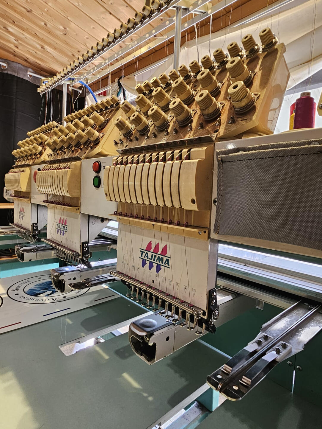 Tête de broderie Tajima multi-aiguilles brodant un logo sur textile à l'atelier Fastnett